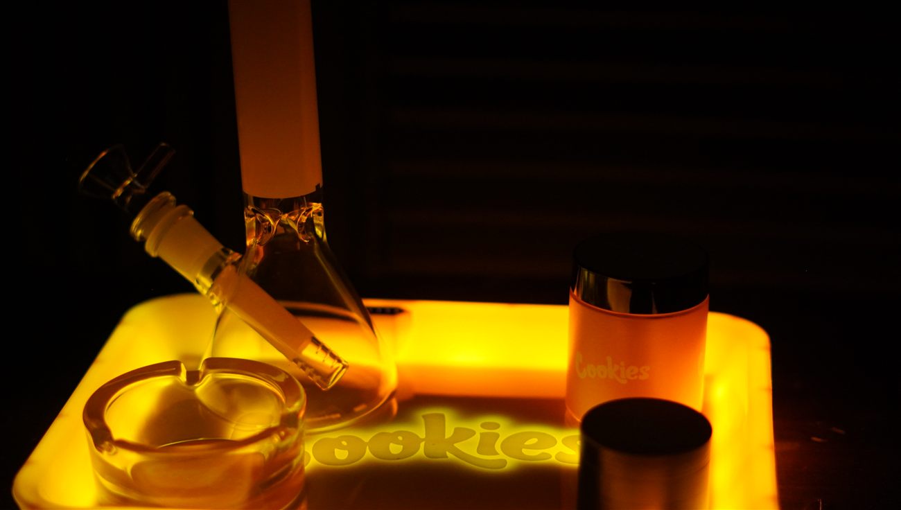 A glowing amber-lit smoking tray with a bong, ashtray, and grinder