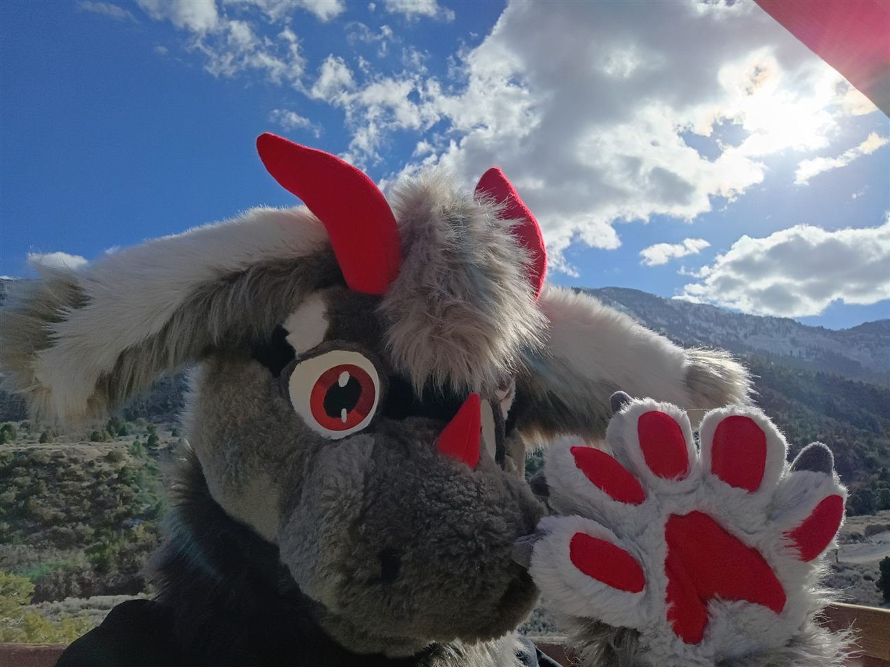 The premade fursuit head with a raised paw showing red claws, mountains in the background