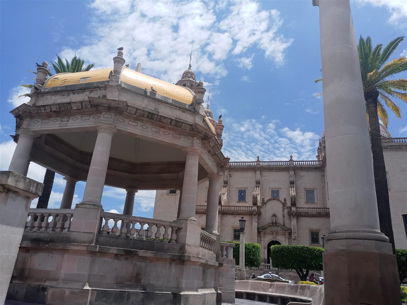 An ornate colonial gazebo with a gold dome, framed by palm trees