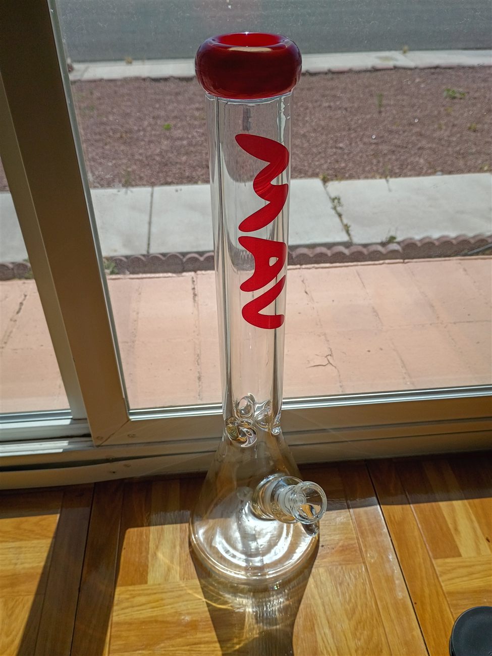 A clear glass bong with a red mouthpiece and the word MAV in red lettering