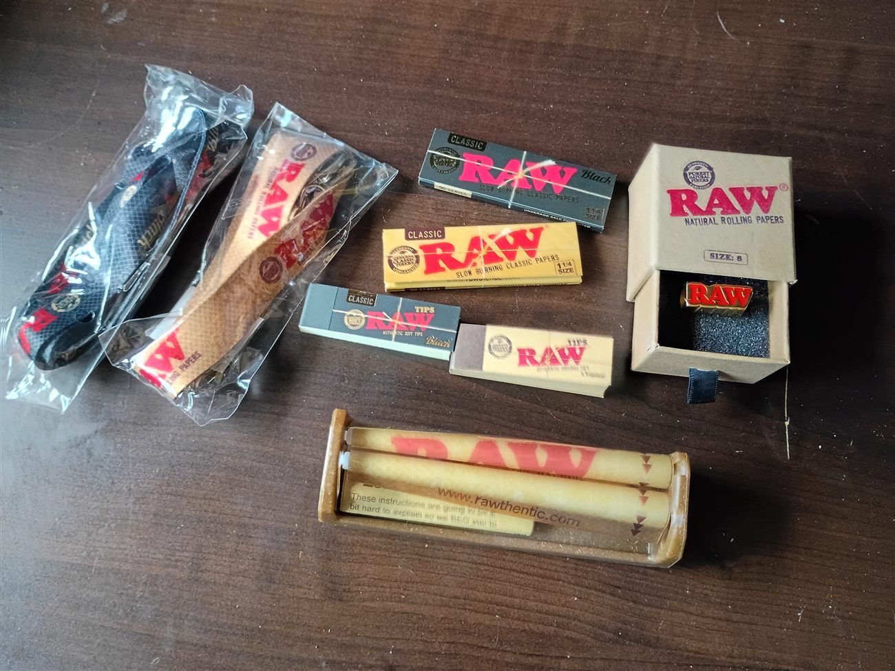 A flat-lay of RAW brand rolling papers, tips, a grinder, and a rolling machine
