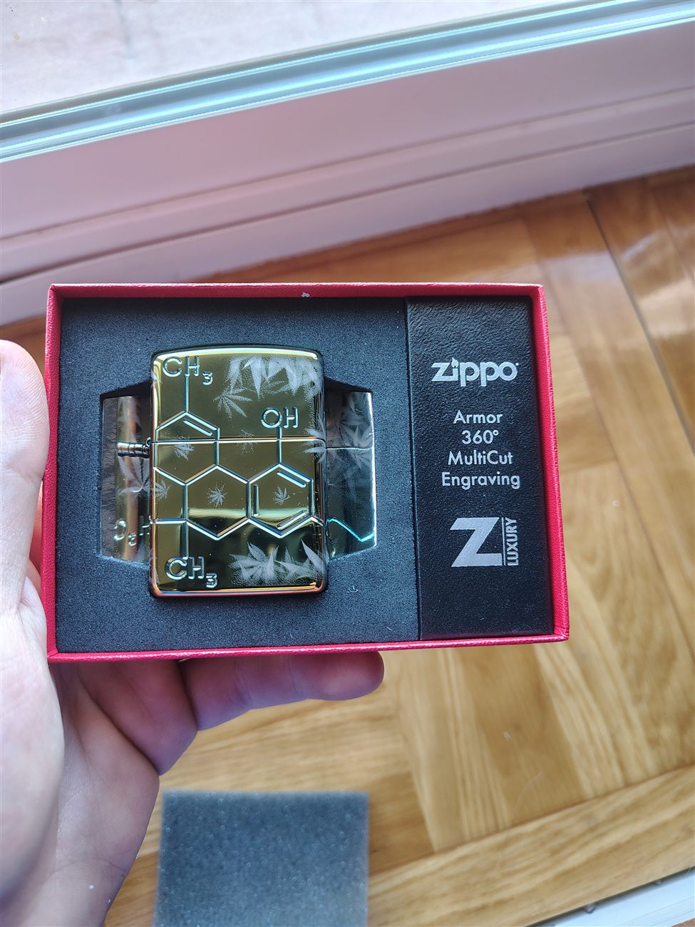 A gold Zippo lighter engraved with a THC molecule and cannabis leaves, in its box