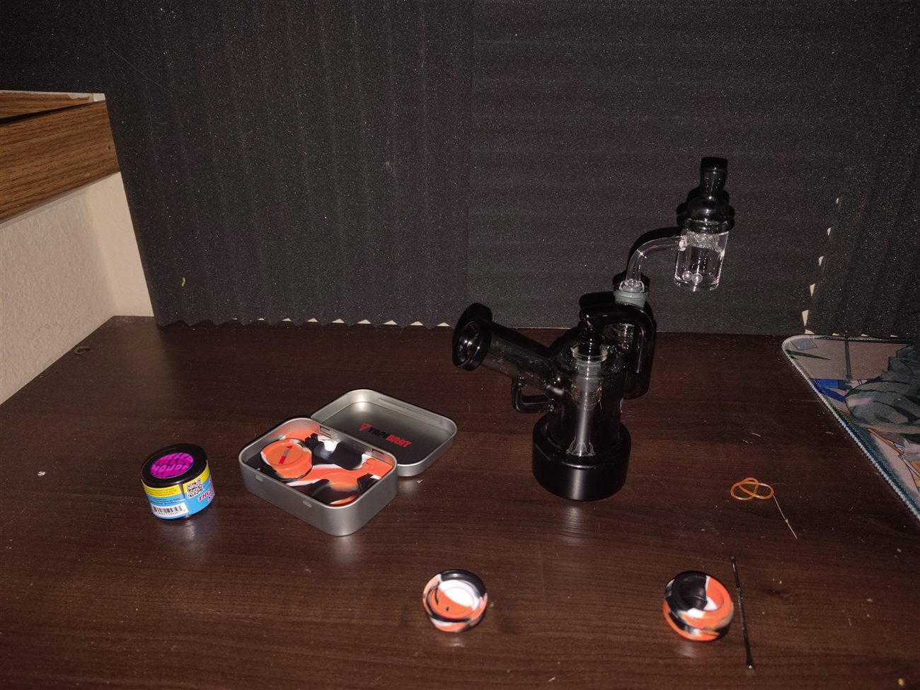 A black glass dab rig set up on a desk with silicone containers