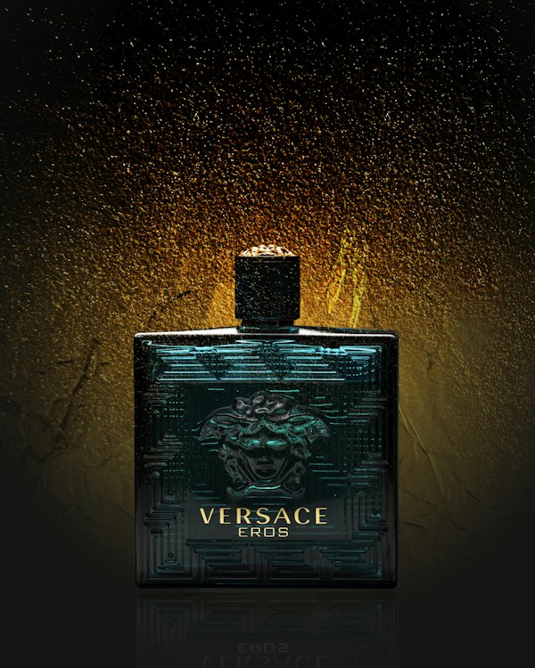 A bottle of Versace Eros against a dark background with gold sparkle