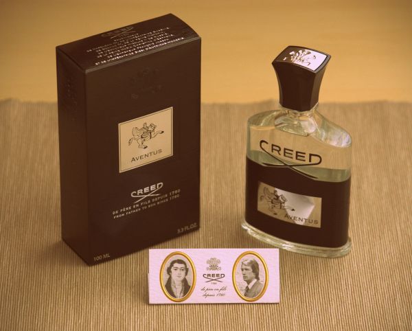 A bottle of Creed Aventus next to its box and a Creed sample card