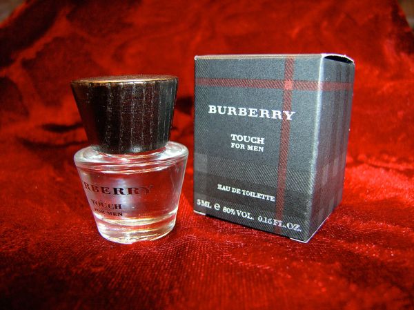 A mini bottle of Burberry Touch for Men beside its box on red velvet